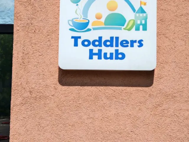 Firmă Toddlers Hub cu grafică colorată și colțuri rotunjite, montată pe fațada roz.