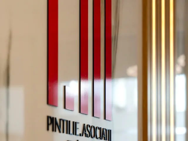 Logo-ul Pintilie Asociații, cu elemente roșii și litere volumetrice negre, montat pe o suprafață vitrată.