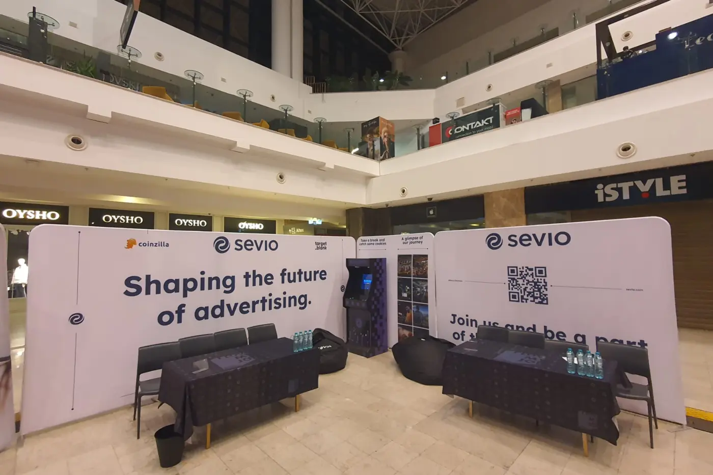 Stand Sevio cu pereți textili curbați, mese și scaune, amenajat într-un spațiu comercial.