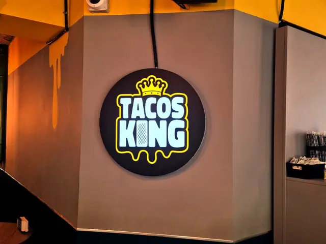 Firmă luminoasă rotundă Tacos King, montată pe peretele interior al restaurantului.